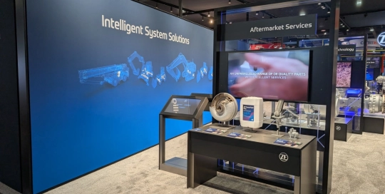 ZF automotive technology on display within the booth, featuring sleek white pedestals and interactive touchscreen monitors for attendee engagement.