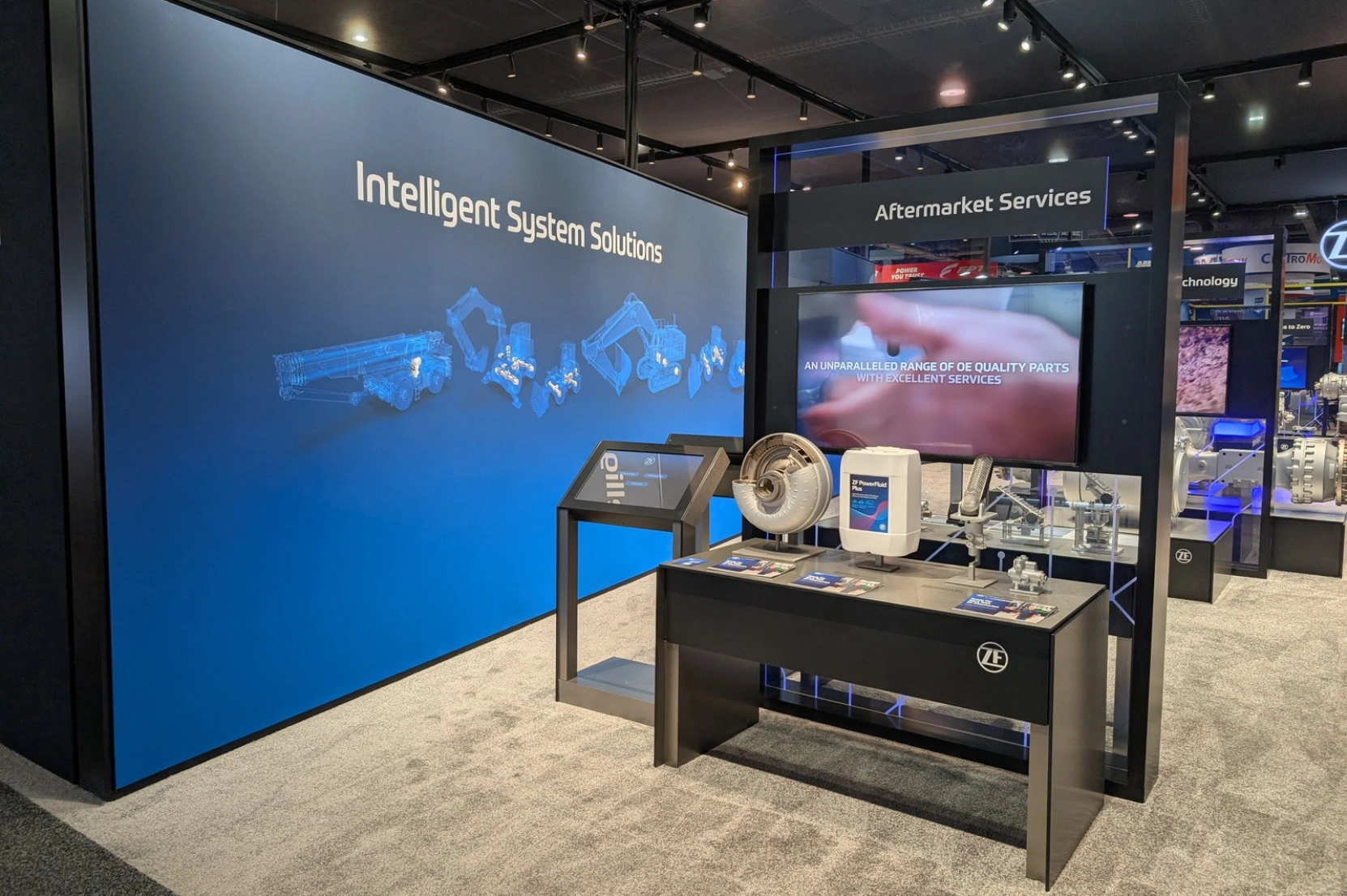 ZF automotive technology on display within the booth, featuring sleek white pedestals and interactive touchscreen monitors for attendee engagement.